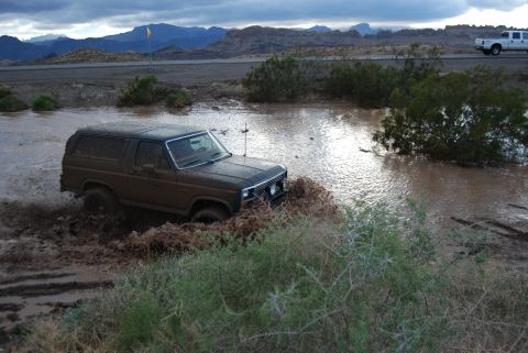 1982 Ford Bronco - Ford Bronco navigates a muddy water obstacle in a desert landscape.