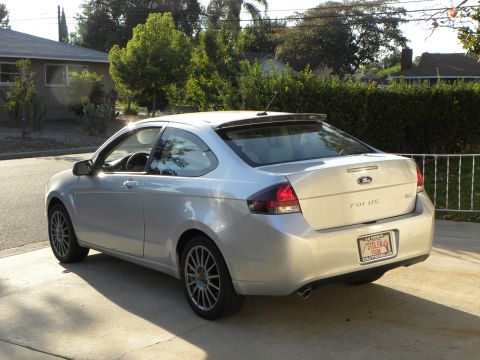 2010 Ford Focus - Rear view of a silver coupe parked on a driveway with a spoiler and aftermarket wheels.