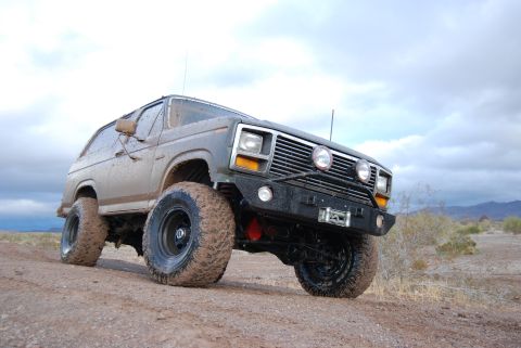 1982 Ford Bronco - This heavily modified SUV, likely from the early 1980s, is shown off-road with large, mud-covered tires and a custom bumper.