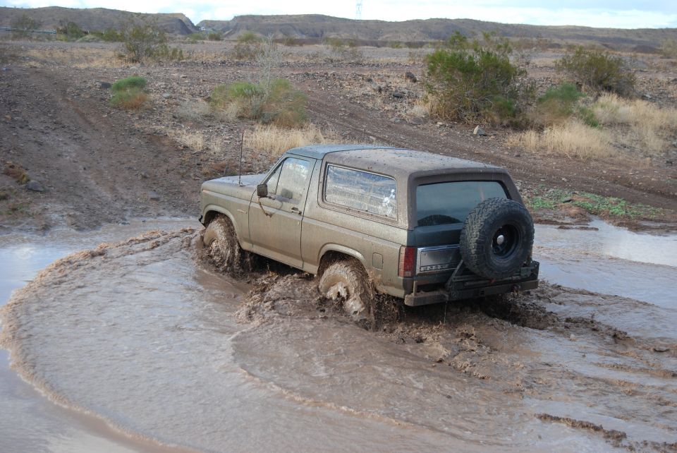 Tan Ford Bronco driving through mud, spare tire on rear door