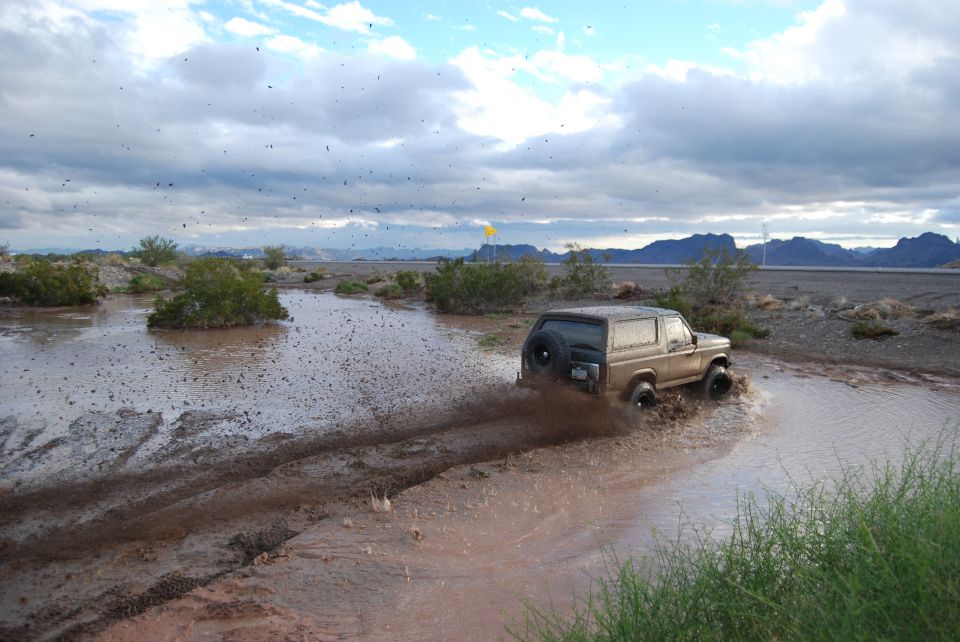 Tan 1982 Ford Bronco driving through mud, kicking up spray