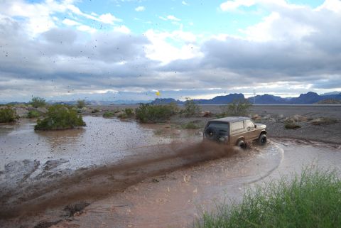 1982 Ford Bronco - Ford Bronco navigates a muddy water obstacle in an arid landscape.