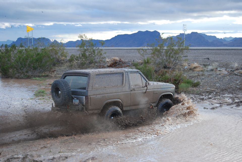 1982 Ford Bronco driving through muddy water, spare tire on back