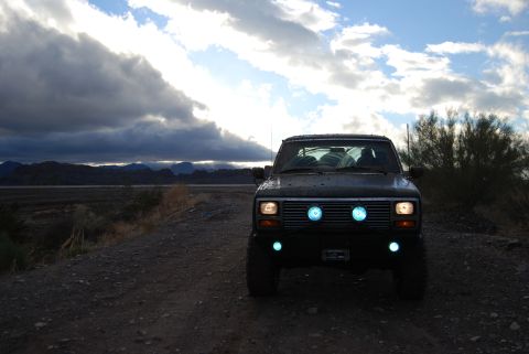 1982 Ford Bronco - Ford Bronco with custom blue lighting sits on a dirt road under a dramatic sky.