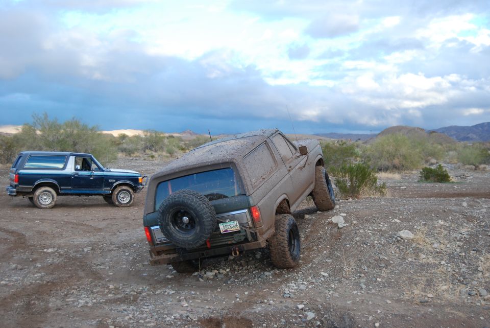 Two Ford Broncos driving on a dirt trail in a desert landscape