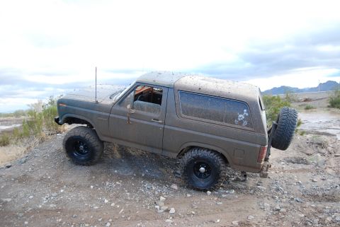 1982 Ford Bronco - This off-road vehicle navigates a rocky and muddy terrain under an overcast sky.