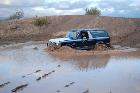1982 Ford Bronco - A dark blue and white Ford Bronco navigates a muddy obstacle course.