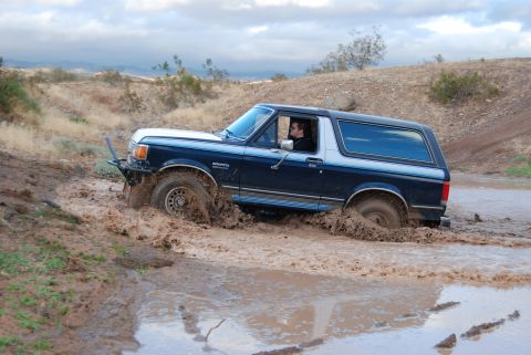 1982 Ford Bronco - A Ford Bronco navigates a muddy trail, with its front tires deep in the mire.