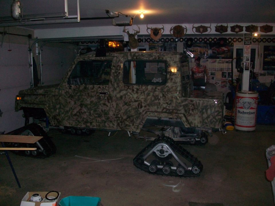 Camo-painted vehicle with track conversion in a garage, spare track on floor