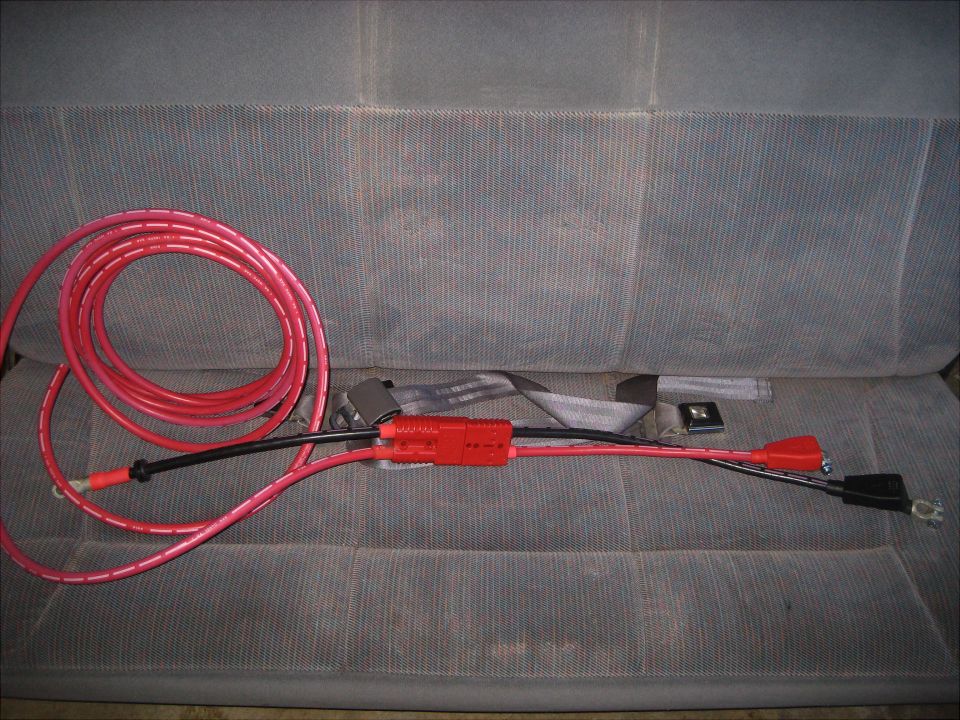 Red battery cables with a red fuse holder and black connectors laid across a gray seat
