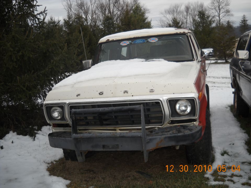 Front view of a white and red 1979 Ford truck with snow on the hood and a brush guard