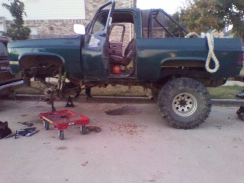 1995 Ford Bronco - This green pickup truck is undergoing repairs with its front end disassembled and supported by jack stands.