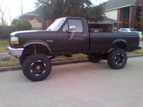 1995 Ford Bronco - A lifted dark pickup truck is parked on a residential street.