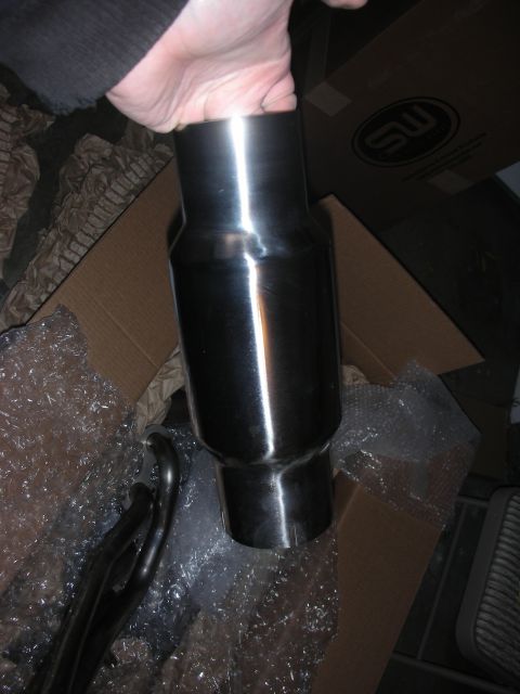 2004 Ford Crown Victoria - A hand holds a shiny exhaust muffler next to a set of headers in a box.