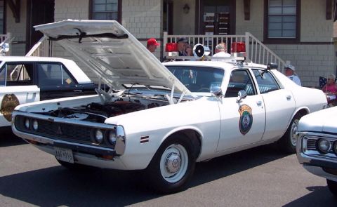 1991 Ford LTD Crown Victoria - White early-1970s Dodge Coronet police sedan photographed from the front three-quarter with its hood propped open at a car show, showing du…