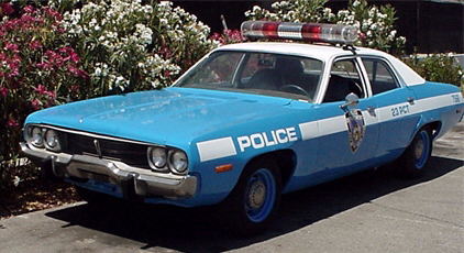 1991 Ford LTD Crown Victoria - Light blue and white 1970s Plymouth Satellite police sedan viewed from the front three-quarter in front of flowering pink oleander, with "P…