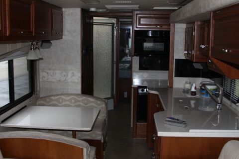2003 Ford F-350 - The interior of a motorhome shows a dinette area, a kitchen with a sink and microwave, and a door leading to the bathroom.