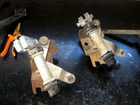 1996 Ford Bronco - Two mechanical parts with mounting brackets and fasteners are laid out on a dark surface.