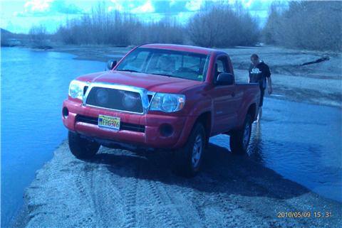 2009 Toyota Tacoma - A red 2009 Toyota Tacoma is parked on a dirt path next to a body of water.