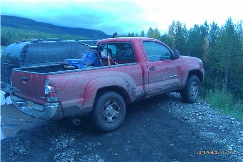 2009 Toyota Tacoma - Red 2009 Toyota Tacoma pickup truck is parked next to a dark SUV in a muddy area.