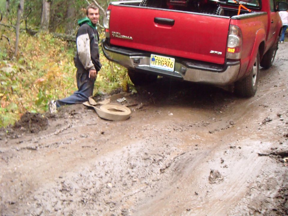 Red 2009 Toyota Tacoma stuck in mud with a man nearby
