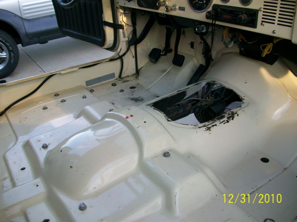 Interior of a stripped-down Jeep, showing the floor pan and dashboard. Another SUV is parked nearby