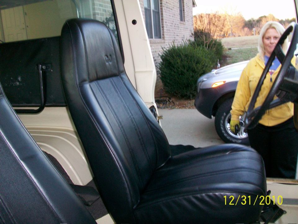 Interior shot of a Jeep with black seats, woman standing by steering wheel, another car parked outside