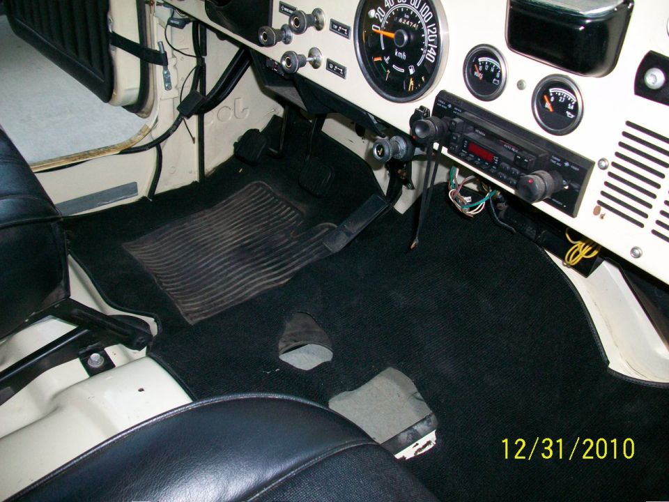 Jeep interior with black carpet and seats, showing dashboard gauges and radio