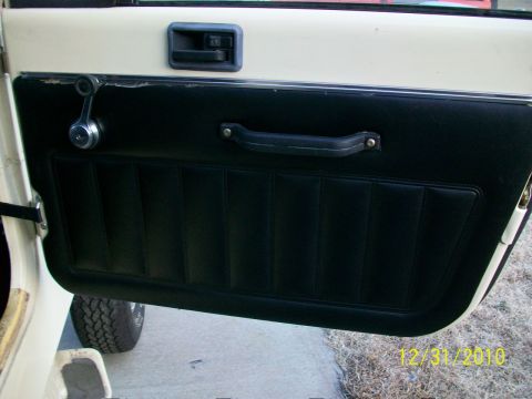 1986 Jeep Wagoneer - Close-up of a vehicle's interior door panel, showing the window crank and handle, with a tire visible below.