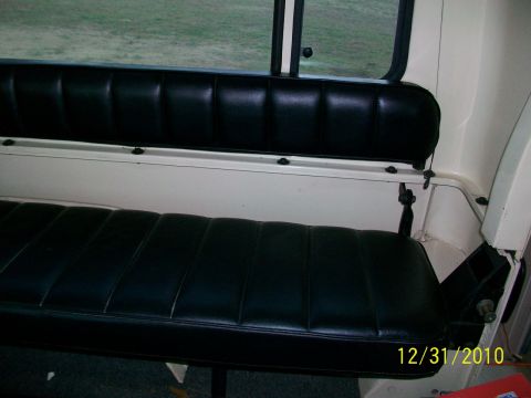 1986 Jeep Wagoneer - The interior of a vehicle shows a black vinyl bench seat with white trim and a window in the background.