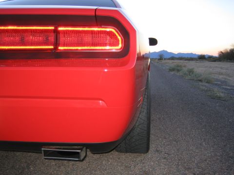 2010 Dodge Challenger - Rear view of a red 2010 Dodge Challenger on a desolate road at dusk, highlighting its distinctive LED taillights and exhaust.