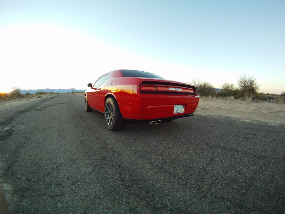 Red Dodge Challenger coupe from low rear angle on desert road at dusk