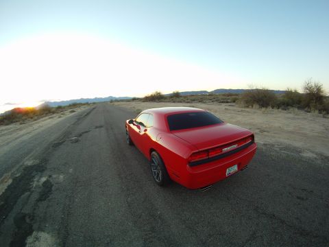2010 Dodge Challenger - A red Dodge Challenger sits on a desolate road as the sun sets in the background.