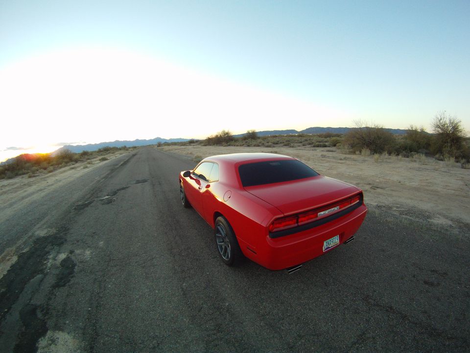 Rear view of a red Dodge Challenger on a cracked desert road at sunrise