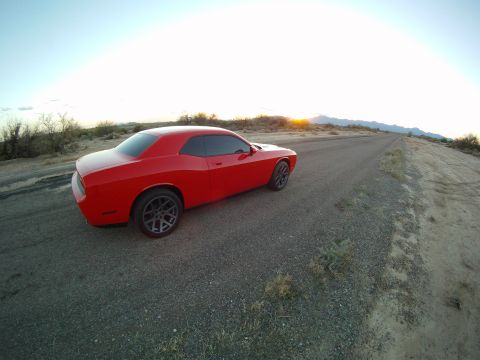 2010 Dodge Challenger - A red 2010 Dodge Challenger is captured in a 3q-front view on a desolate dirt road as the sun sets in the background.