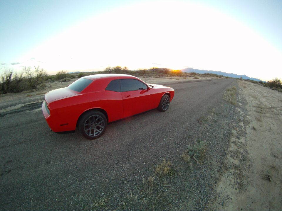 Red Dodge Challenger coupe on an empty desert highway shoulder at sunrise