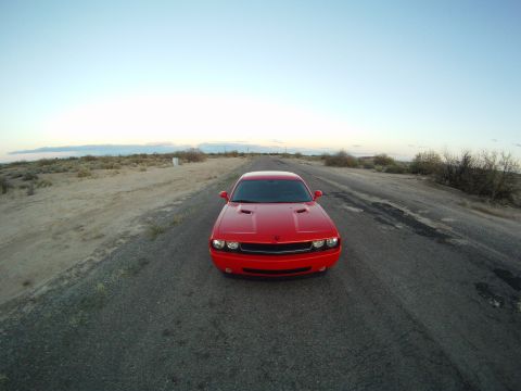 2010 Dodge Challenger - A red Dodge Challenger is seen from the front on a long, empty road under a clear sky.