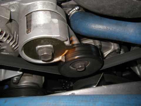 1990 Ford Bronco - Close-up view of a fan belt tensioner assembly, showing a pulley and a metal plate with 'RANGE' inscribed.