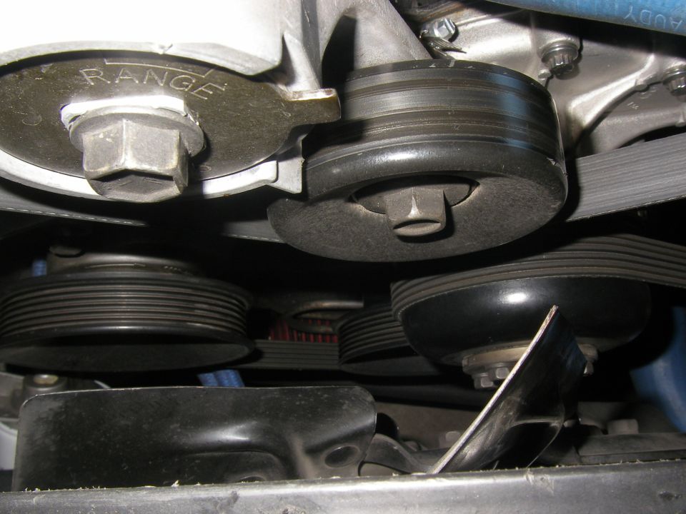 Close-up of engine belt tensioner with 'RANGE' visible on a metal plate, and multiple pulleys and belts