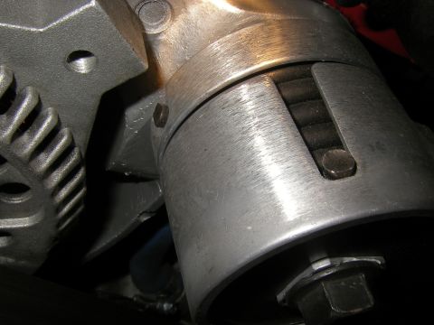 1990 Ford Bronco - Close-up of a metal fan belt tensioner assembly, showing its ribbed pulley and adjustment bolt.