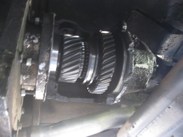 Opened gearcase under a truck showing two oily helical gear clusters and bearings