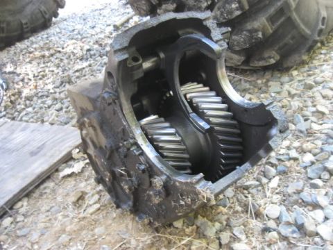 1982 Ford F-100 - A cast-iron transfer case sits open on gravel with its rear housing removed, exposing the wide helical planetary gearset and output shaft s…