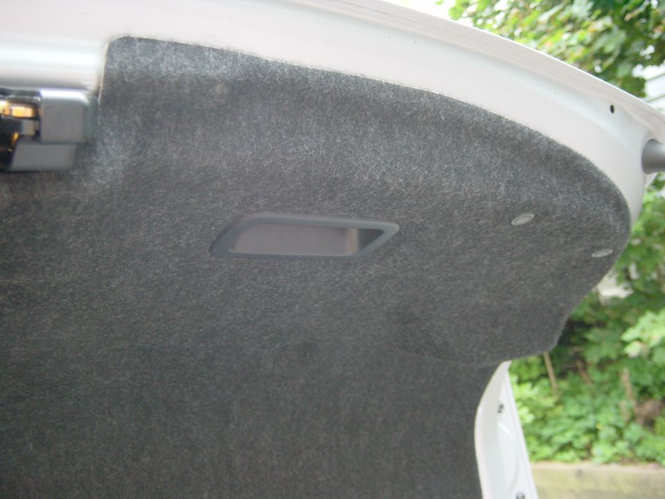 Underside of open trunk lid with gray felt lining and white painted edge, outdoors