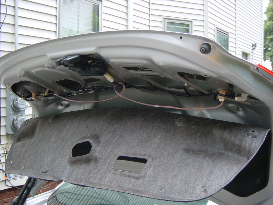 Underside of open silver sedan trunk lid with exposed wiring and routed red wire
