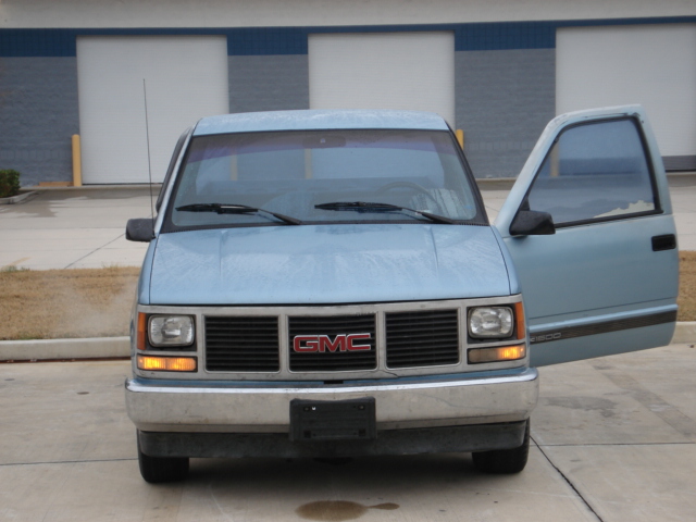 Front view of a light blue GMC pickup truck with the driver's door open. It has a black grille with a red GMC badge