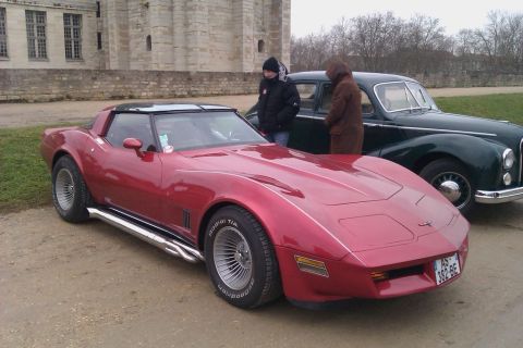 1991 Ford Crown Victoria - A red Chevrolet Corvette is parked in front of a building with another car behind it.