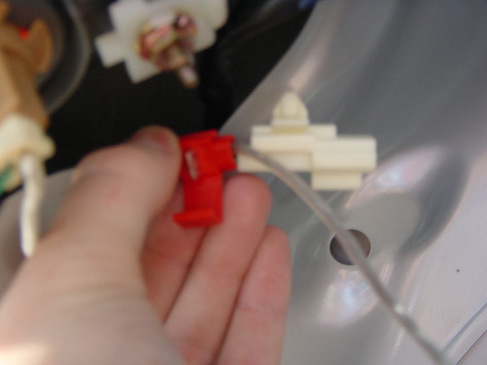 Hand holding red electrical connector near white connector on gray plastic panel