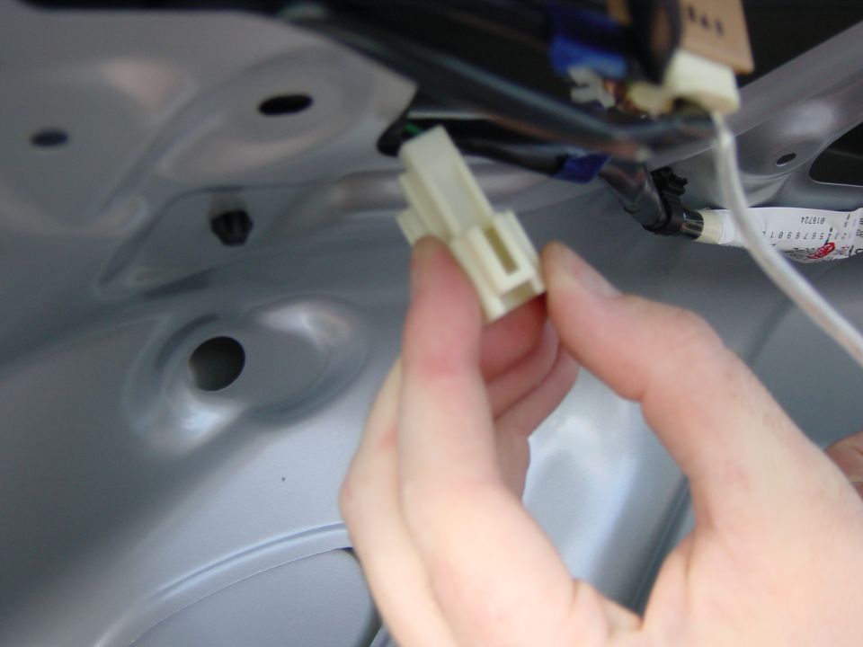 Hand disconnecting a tan plastic wiring harness connector against gray body panel