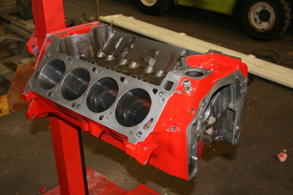 Red painted engine block on a red stand, showing four cylinder bores