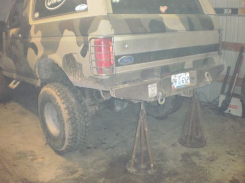 1995 Ford Bronco - The rear of a Ford Bronco is shown on jack stands, with a camouflage paint scheme and a visible license plate.